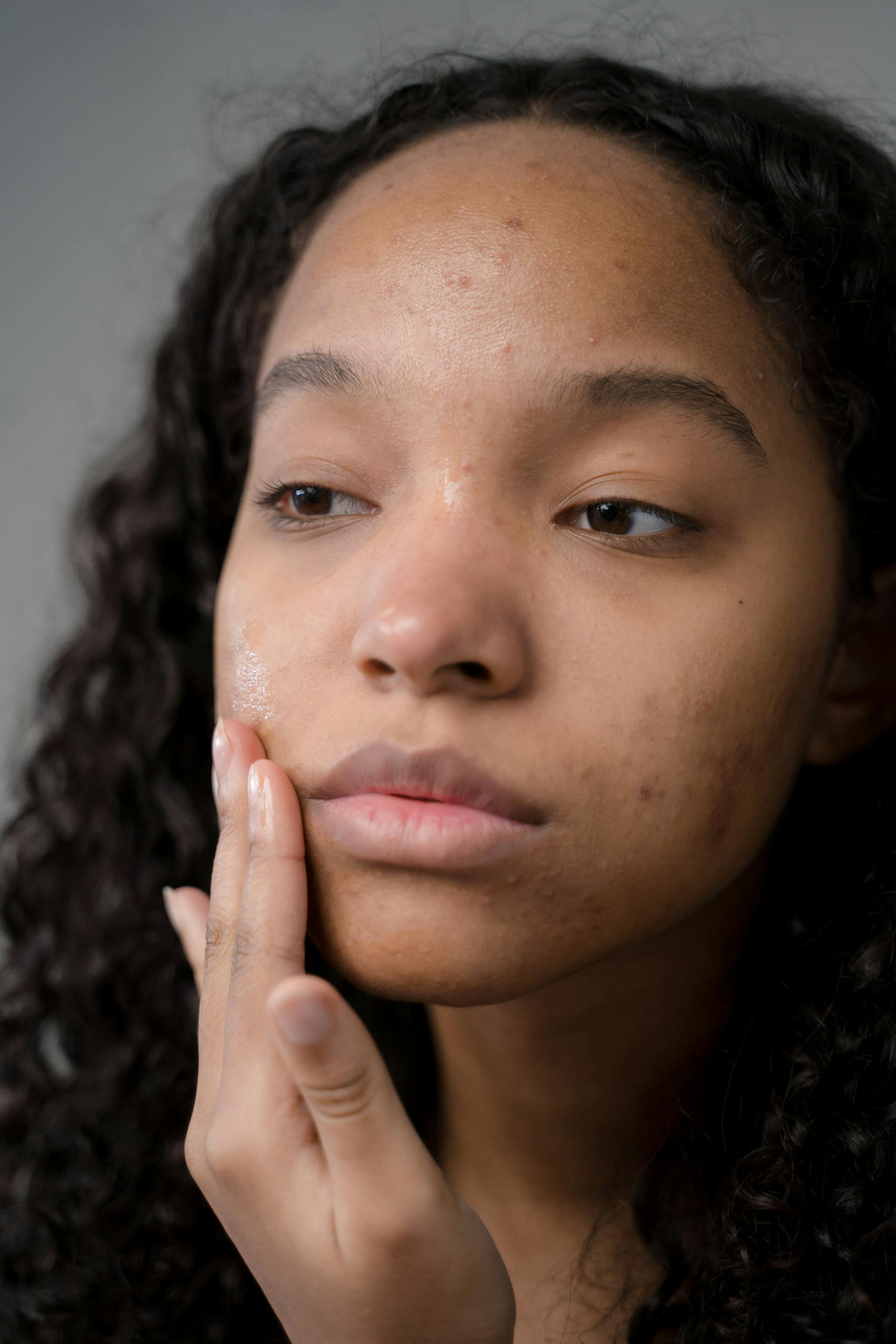 A thoughtful woman with curly hair examines her skin condition during a skincare routine.